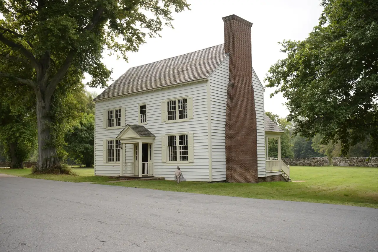Rendered image of a historic white frame house with a brick chimney on a village lane