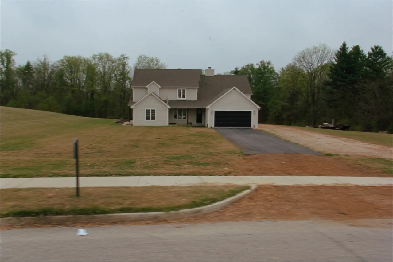 Rendered image of a two-story house on a large open lot with woods behind