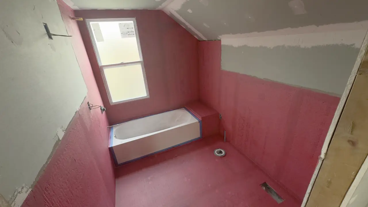 Tub surround and floor coated in red liquid waterproofing membrane before tile.