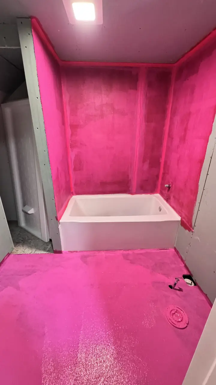 Shower walls and pan coated in pink liquid membrane, tub set, before tile.