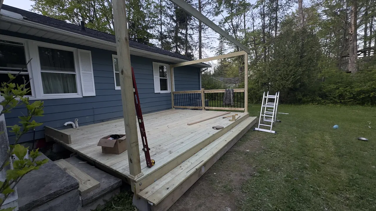 Framed deck platform with railing posts set, a ladder against the house.