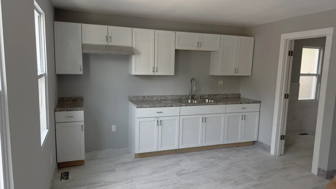 Finished kitchen with white shaker cabinets, a granite counter and a grey plank tile floor.