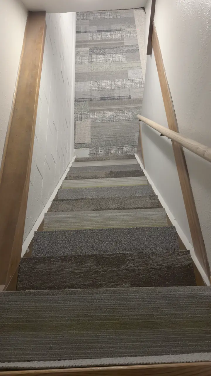 Basement stairs with a striped carpet runner and a new wood handrail.