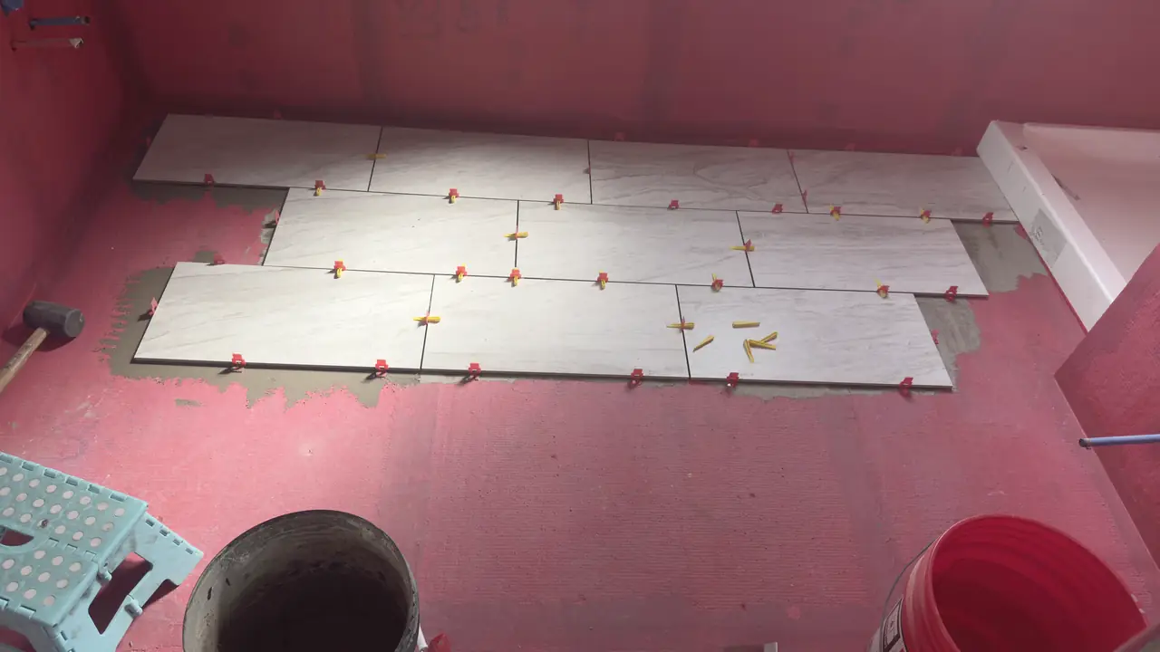 Plank tile laid out on red membrane with spacers, tub at the back.