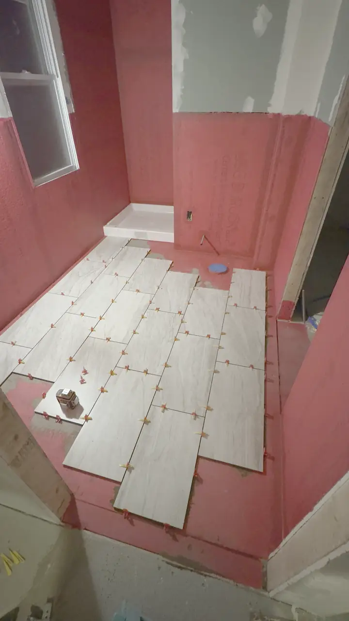 Plank floor tile set with orange spacers, tub in place, walls still red membrane.