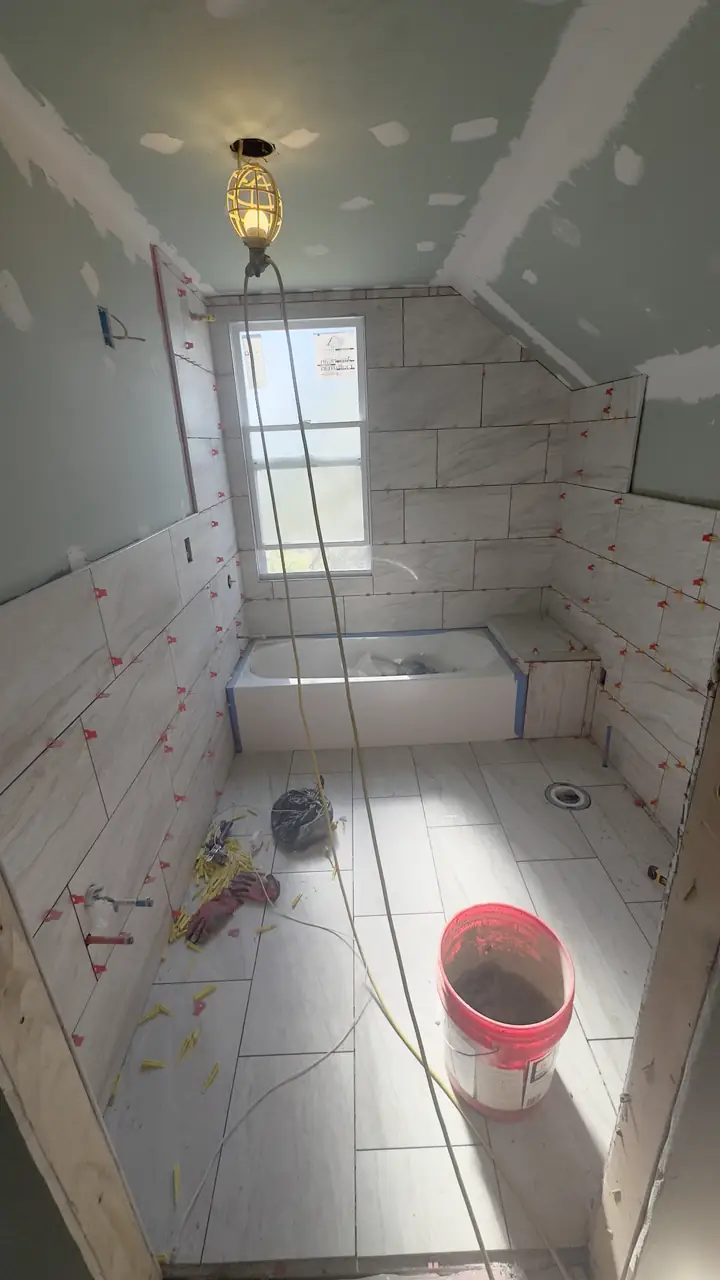Large-format wall tile going up around the tub, spacers still in.
